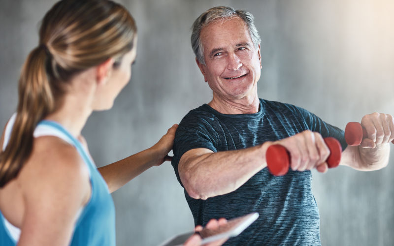 An adult strengthening with dumbbells and physiotherapy support